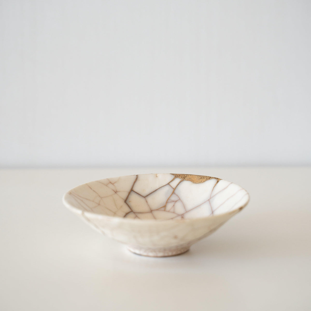 Bol en céramique blanche réparé avec du kintsugi, art traditionnel japonais de réparation de poterie brisée avec de la laque dorée, mettant en valeur la beauté de l'imperfection et embrassant le concept de wabi-sabi.
