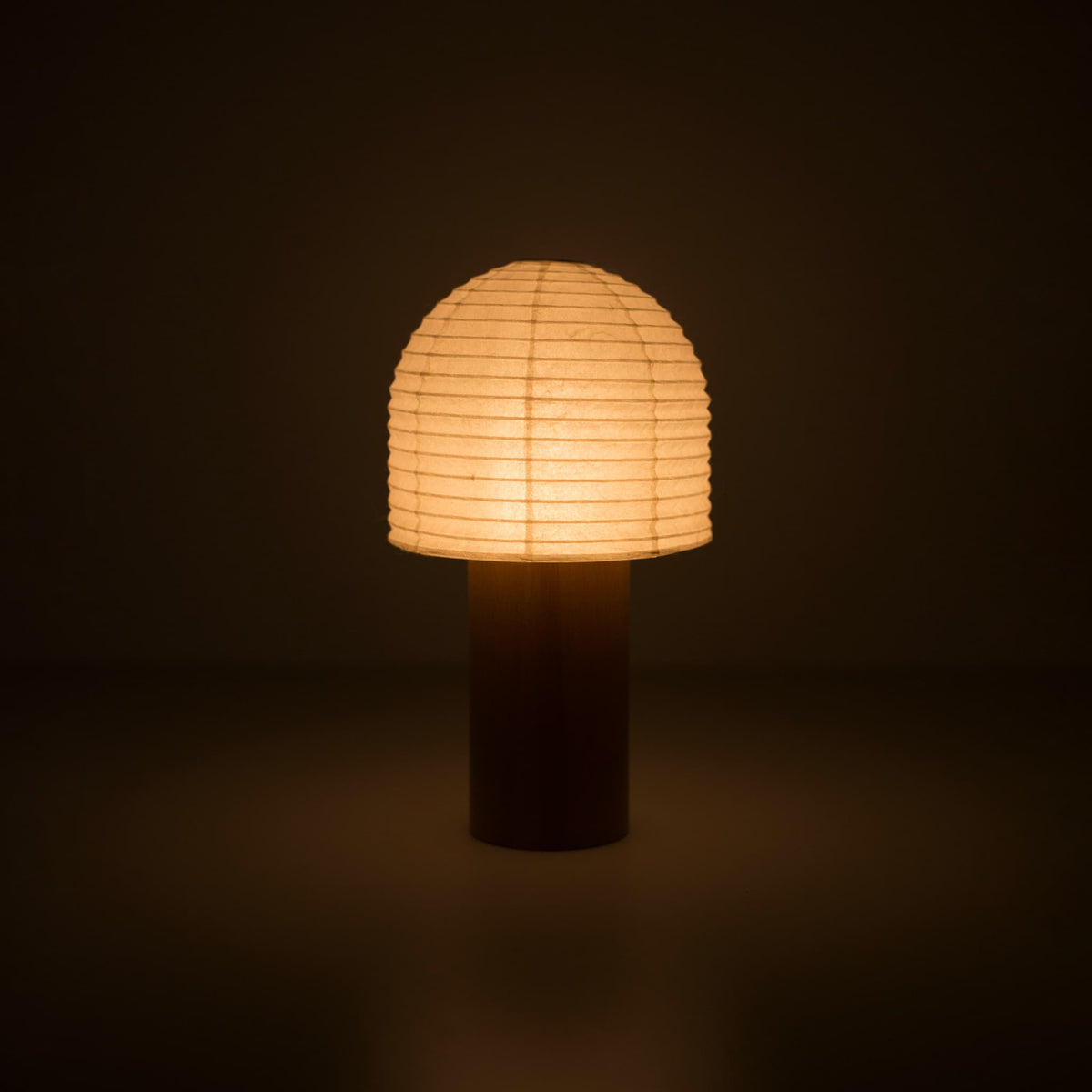 Een draagbare Japanse papieren lantaarn met een houten handvat en een klokvormige bovenkant, die warm gloeit in een donkere kamer