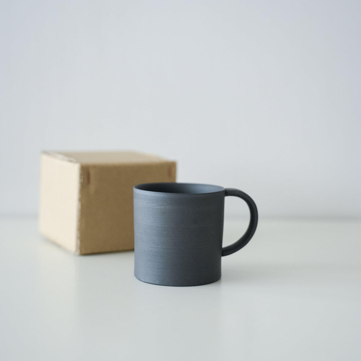 Eine schlichte schwarze Banko-Keramik-Tasse in einer minimalistischen Papierbox.