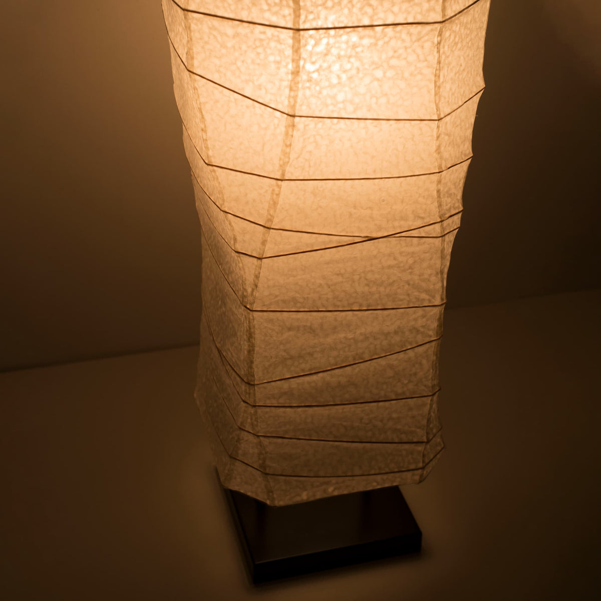 Gros plan sur la partie inférieure d'une lampe japonaise en papier washi, vue de dessus, mettant en valeur ses courbes élégantes et sa lumière chaude