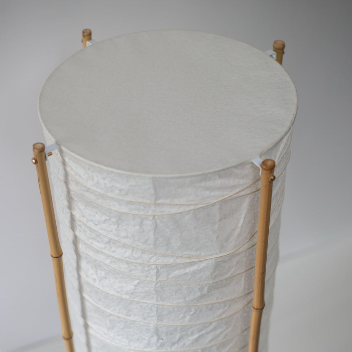 Close-up of the top section of a cylindrical Japanese lamp with bamboo frame and washi paper, white background