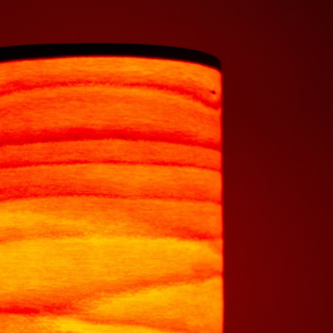 Gros plan d'une lampe de table japonaise cylindrique projetant une lumière semblable à une flamme à travers de fines lamelles de bois.
