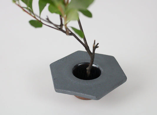 A hexagonal minimalist iron vase inspired by traditional Japanese roof tiles, with a branch arrangement.