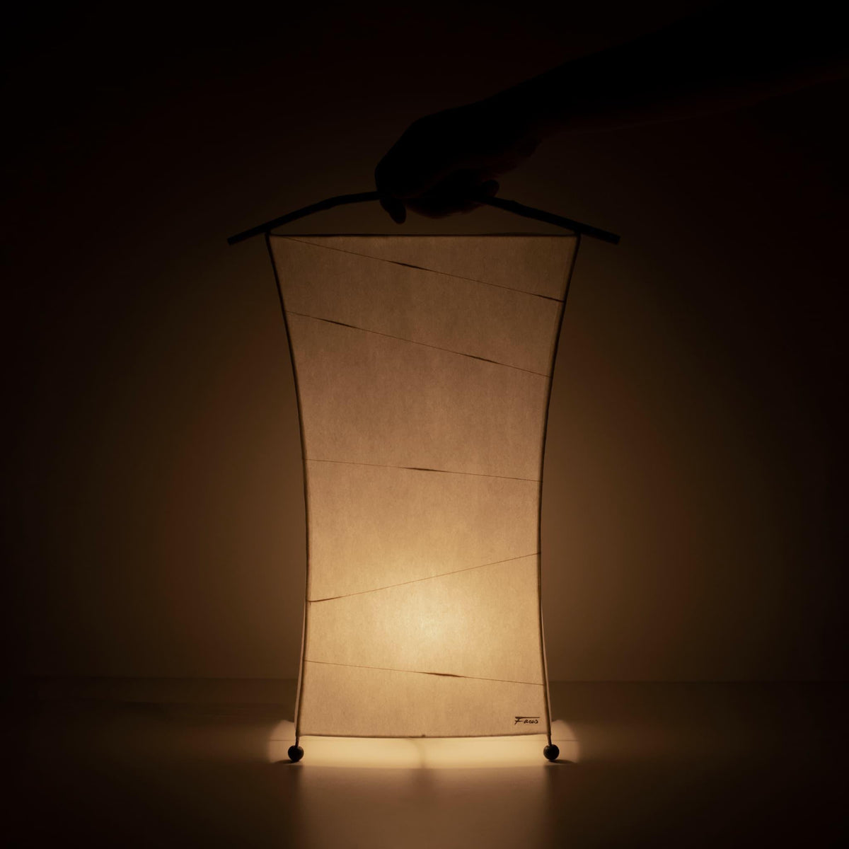 Hand die een unieke papieren staande lamp vasthoudt, vervaardigd met Gifu-lantaarntechnieken en 1300 jaar oud Mino washi-papier.