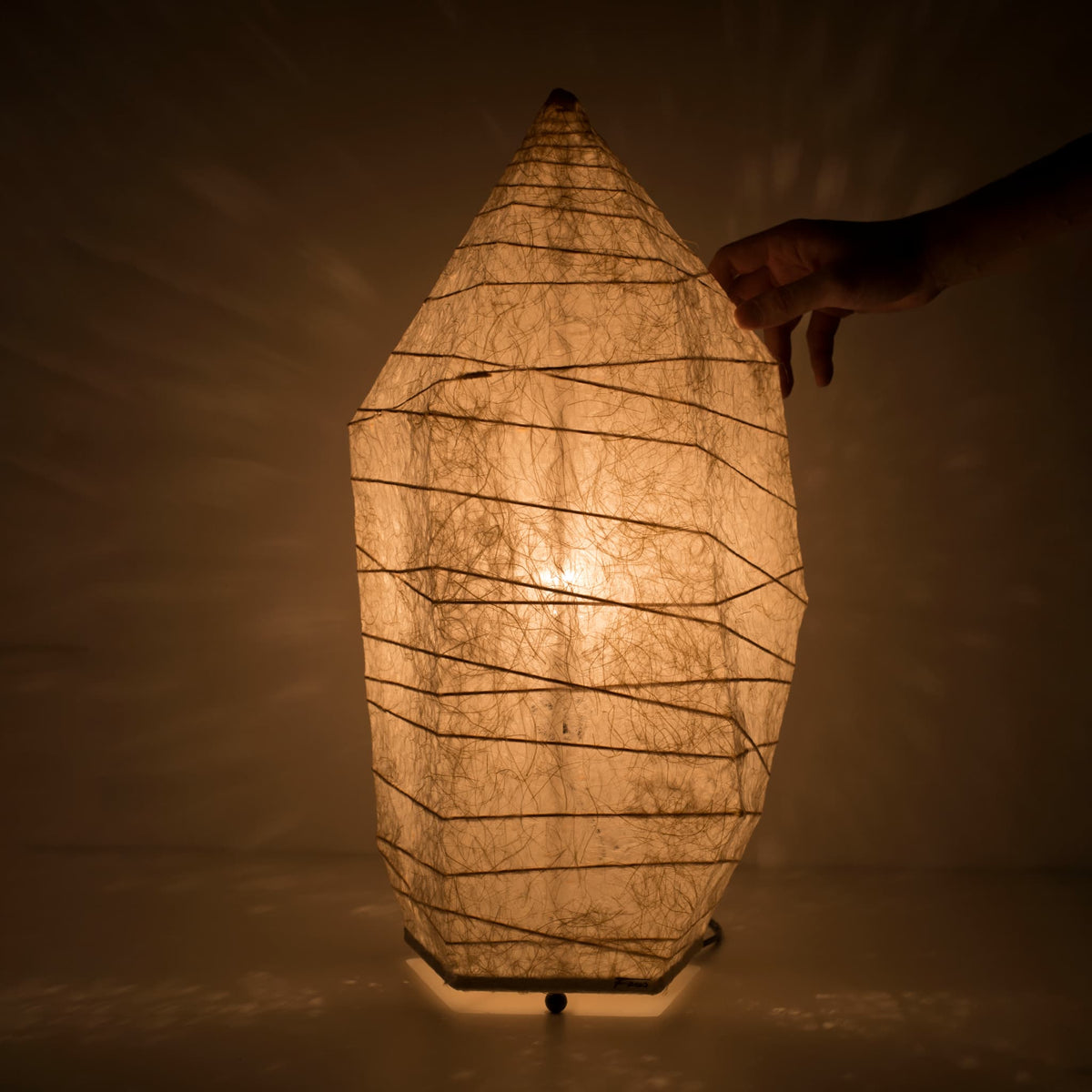 hånd rører ved toppen af en japansk papirgulvslampe med isstensdesign og varm glød, lavet af traditionelt washipapir
