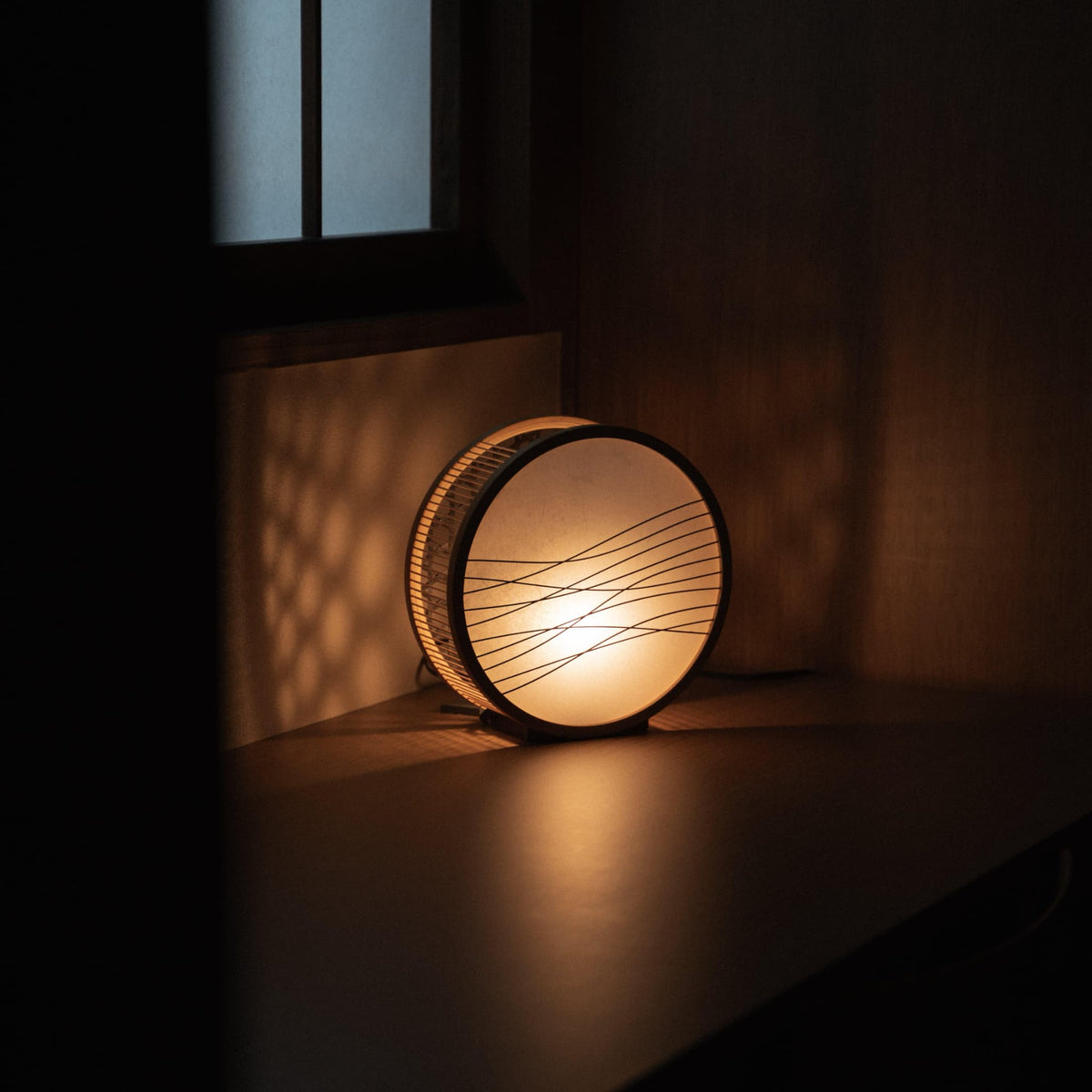 Traditional Japanese bamboo lamp handcrafted in Shizuoka with 800-year-old techniques, casting an ethereal glow on a bedroom table.