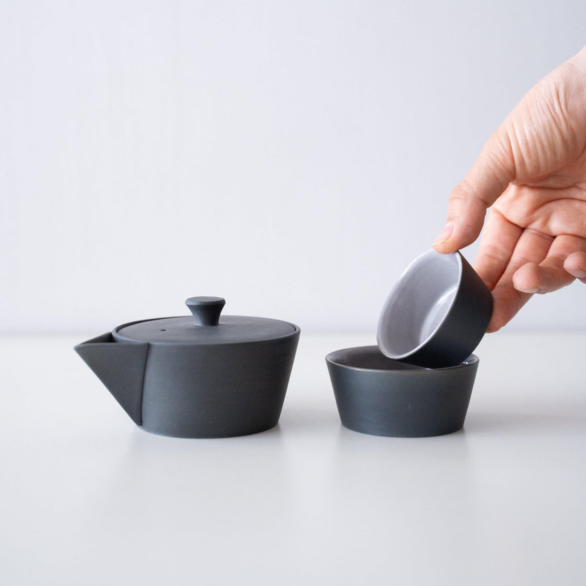 Hånd, der holder en sort japansk Banko-yaki tekande og et sæt med to kopper, med en historie på flere hundrede år.