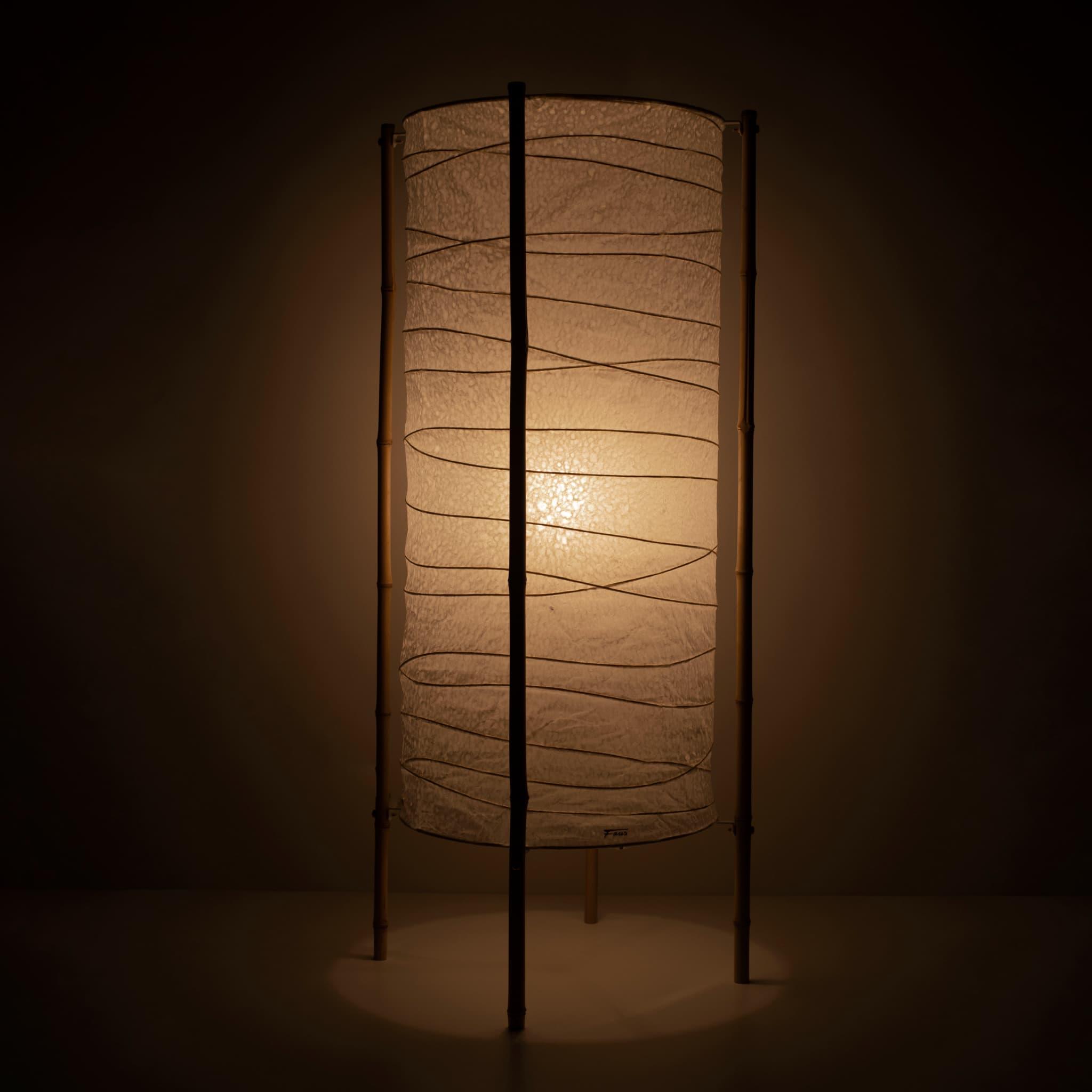 Full view of a Japanese paper lamp with cylindrical washi paper shade and bamboo frame, warm glow on brown background