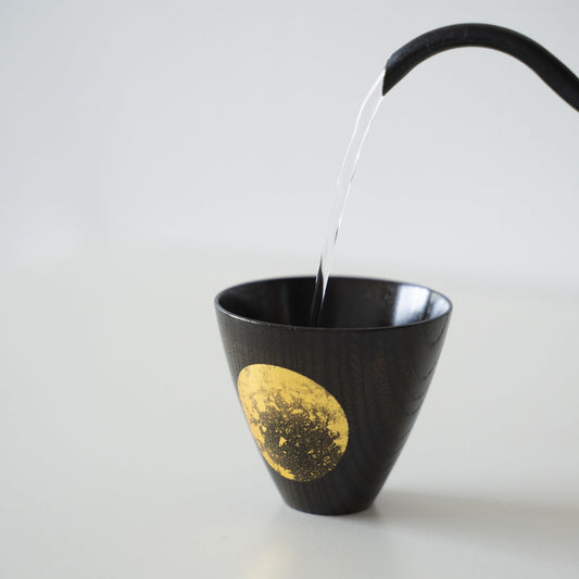 Water wordt in een Japanse lakwerk sake-beker gegoten.