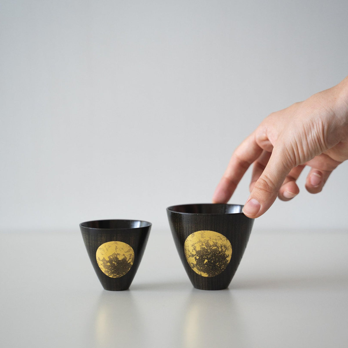 One of the two Japanese lacquerware sake cups placed side by side is being held in hand.