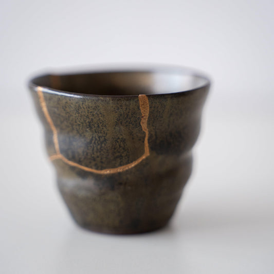 Close-up of a deep green sake cup repaired with Kintsugi, a traditional Japanese technique, showcasing the beautiful golden joinery.
