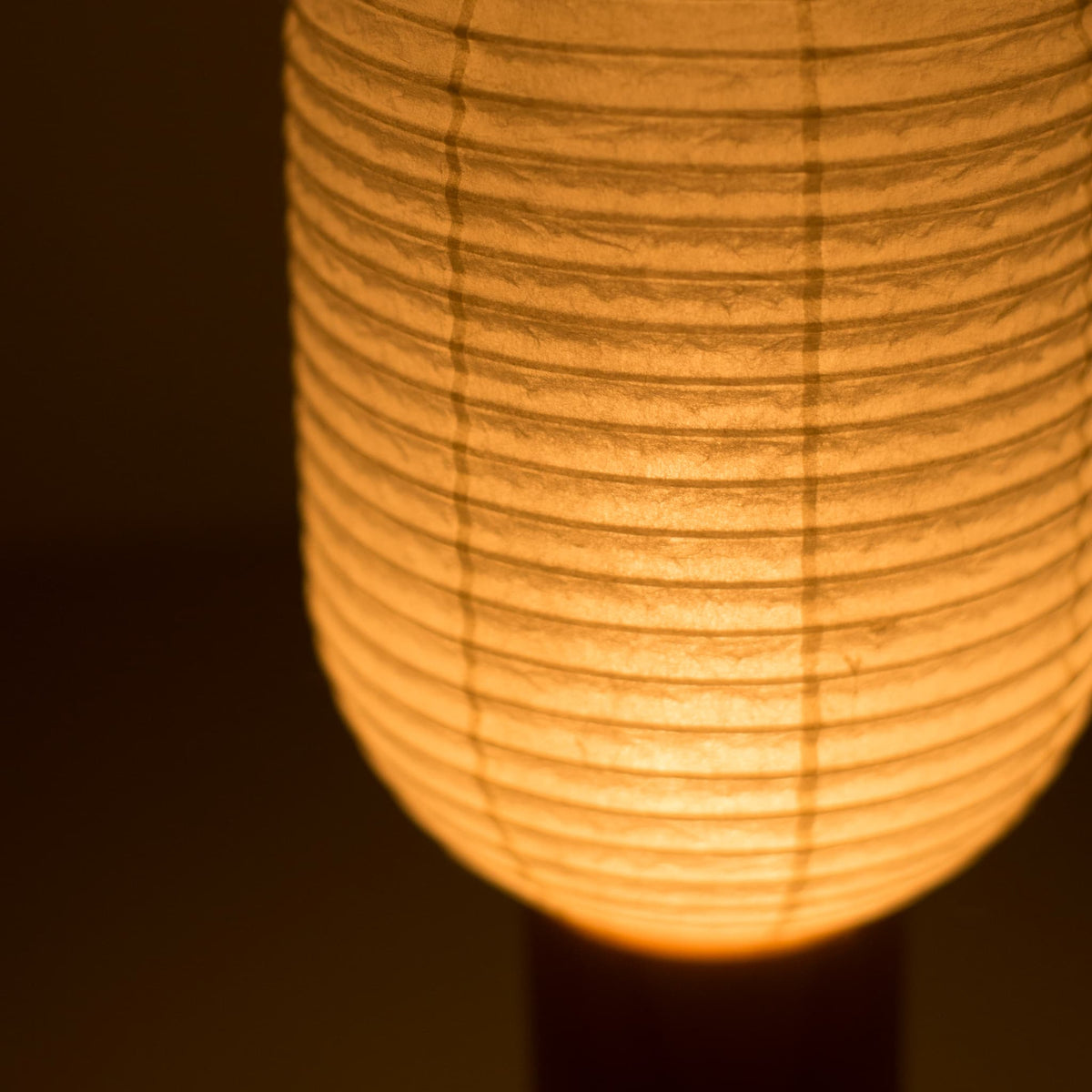 Gros plan de la lanterne japonaise "TORCHIN VERTICAL", mettant en valeur les détails complexes de son abat-jour en papier washi et la lumière chaleureuse qu'elle diffuse.