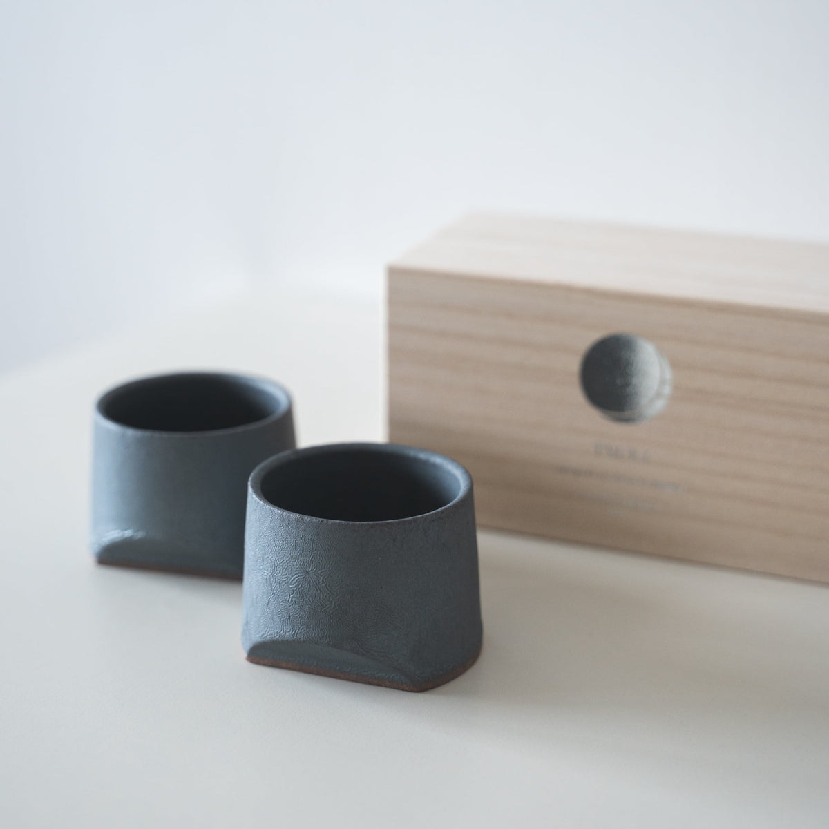 Gift set of two iron-colored sake cups, crafted using traditional Japanese roof tile techniques, presented in a paulownia wood box.