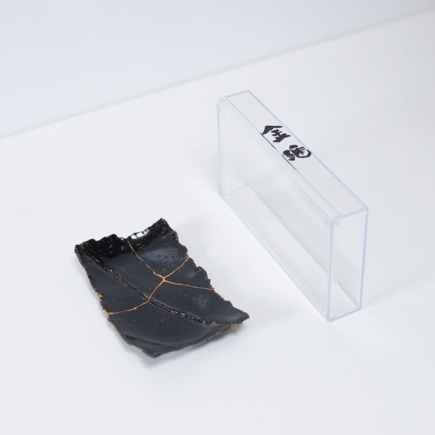 "Kintsugi-bord 'Tenmoku' zwart 01 gepresenteerd met een doorzichtige hoes, bovenaanzicht."