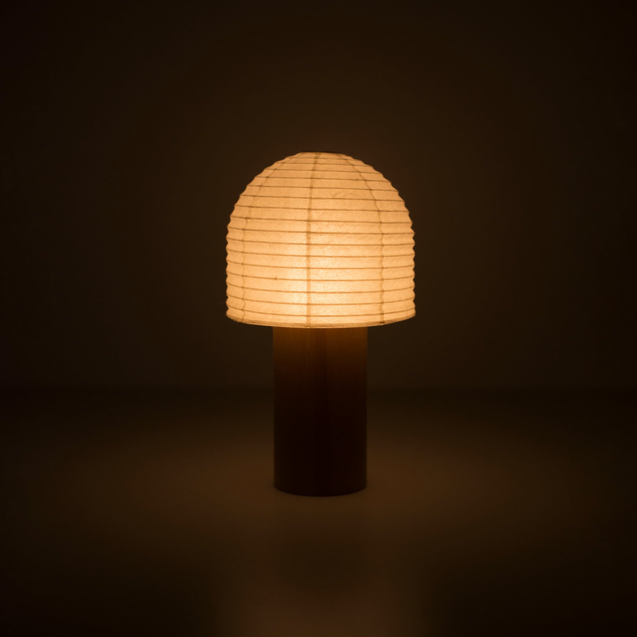 Eine tragbare Papierlampe mit Holzgriff und glockenförmigem zylindrischem Papieraufsatz, die in einem dunklen Raum warmes Licht abgibt