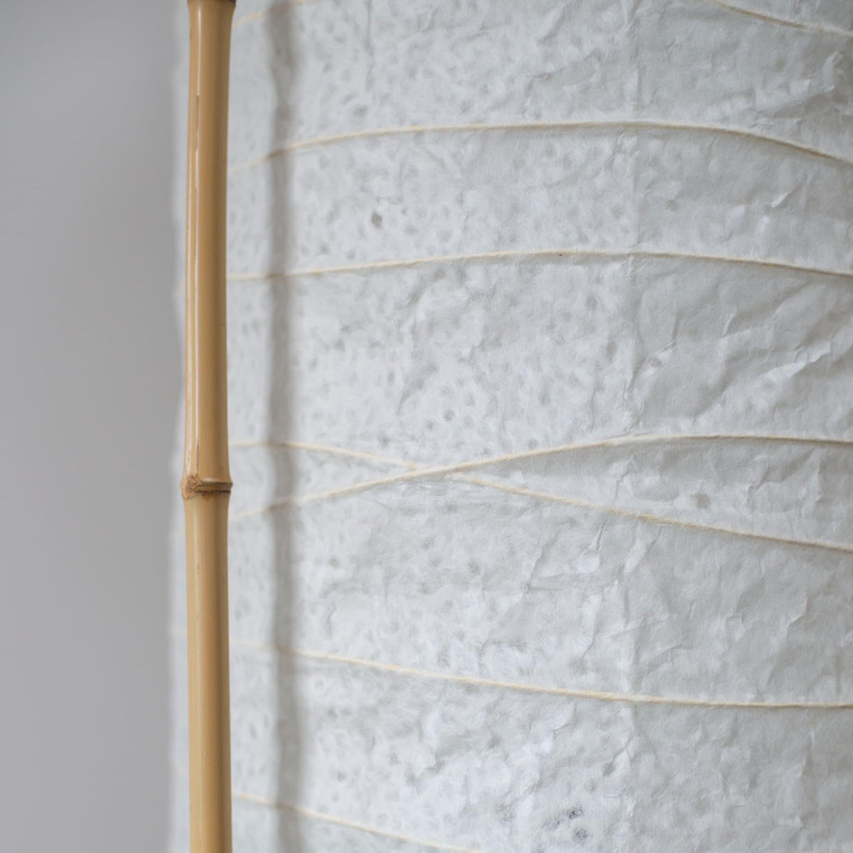 Detailed side view of a cylindrical Japanese lamp, showing the contrast between soft white washi paper and brown bamboo frame
