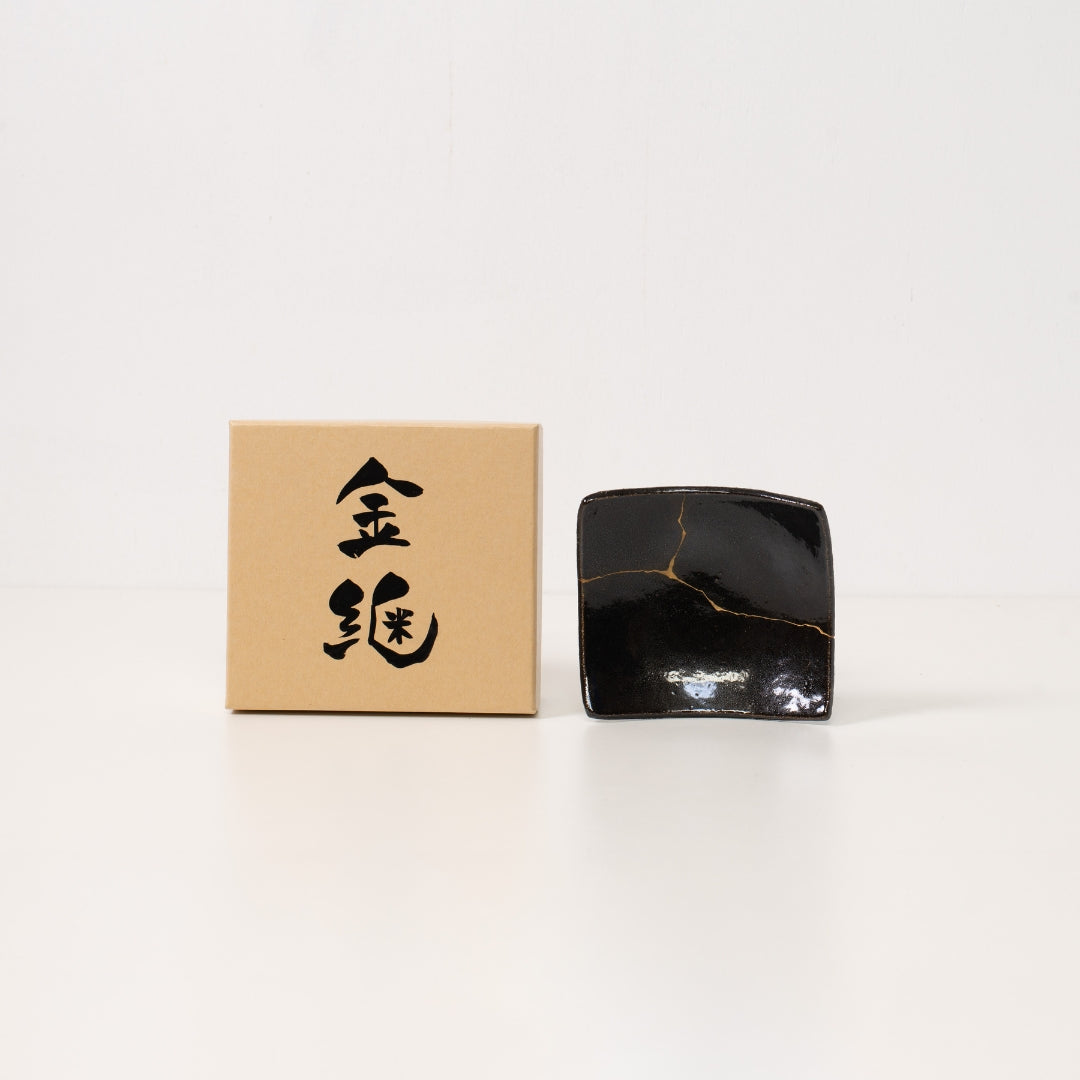 A jet black kintsugi plate sits beside a brown japanese gift box ready to be presented as meaningful wabi sabi art
