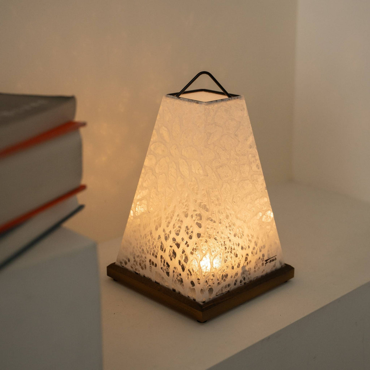 "Mini Akari" witte gloeiende Japanse papieren tafellamp als gezellige papieren lamp-accent naast boeken op een Japandi-woonkamerplank.