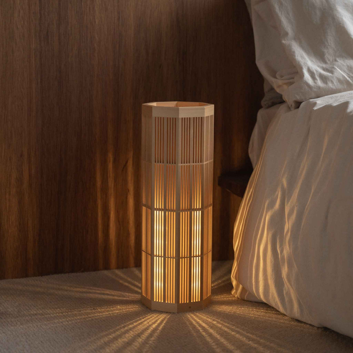 Gezellige Japanse houten vloerlamp "SAN" Groot in een slaapkamer, die helende radiale schaduwen projecteert als sfeerverlichting.