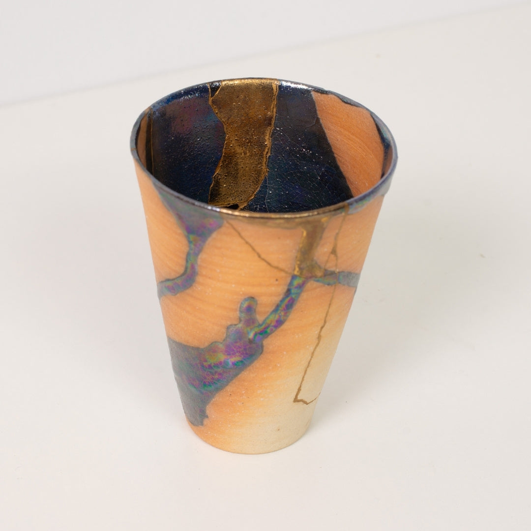 Nærbillede inde i en bred kintsugi-kop, der viser indviklede guldlinjer og mørke glasurer af traditionel keramik