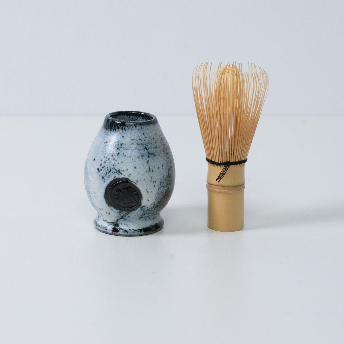 Support en céramique blanc et noir pour fouet à matcha japonais "Creative Cloud", placé à côté d'un fouet à matcha traditionnel en bambou, Japon.
