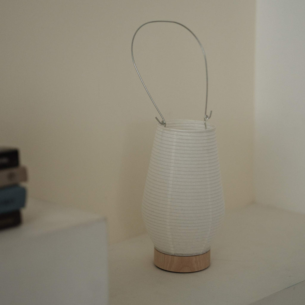 bærbar japansk papirlampe RIN 02 med metalhåndtag, der står på en hvid overflade og viser dens sarte mino washi-tekstur
