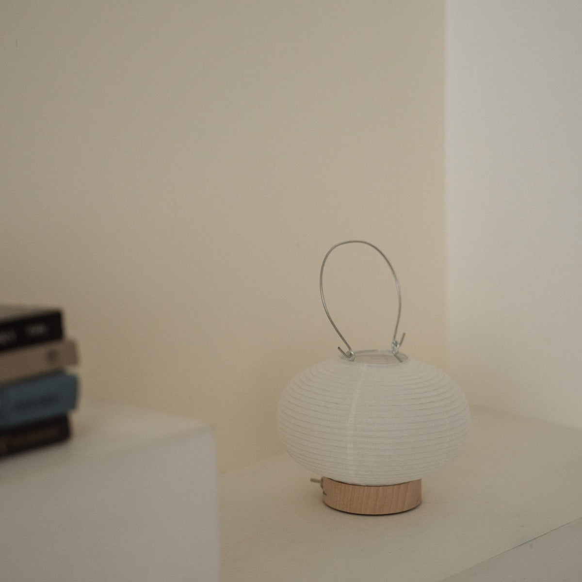 A portable japanese paper lamp RIN 03 with a metal handle sitting on a white surface showing its delicate mino washi texture