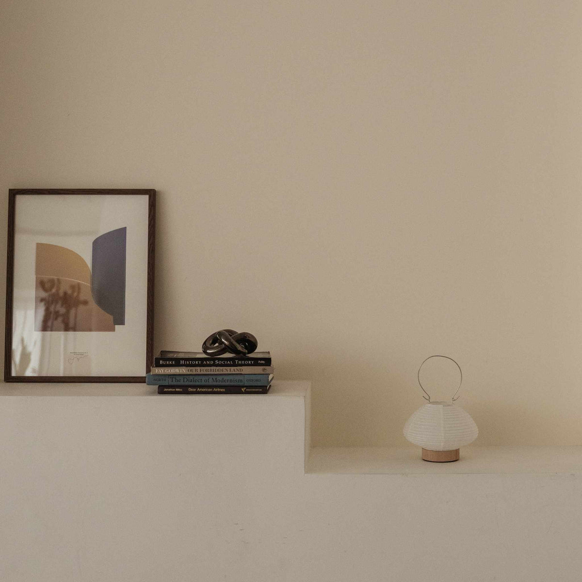 Unlit japanese paper table lamp RIN 01 placed on a white shelf next to books and art in a japandi style room