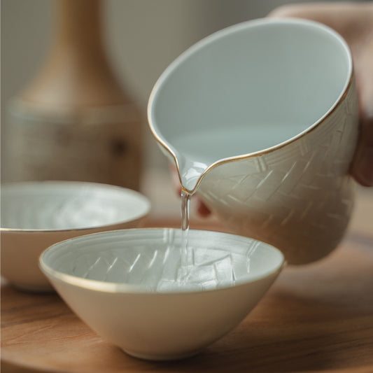 Hand pouring from a white Japanese sake pitcher into a delicate guinomi cup on a wooden tray, elevating a special dinner.
