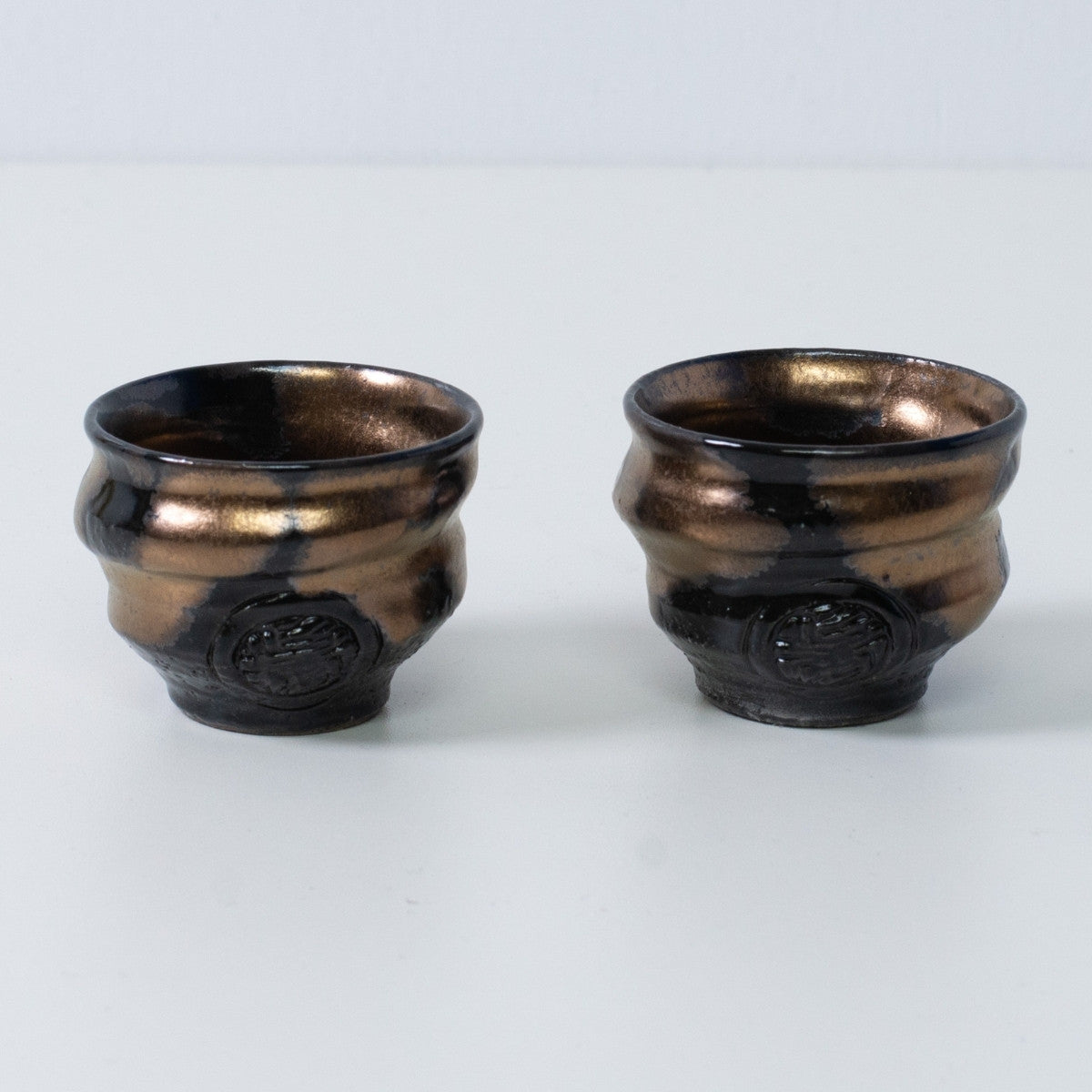 Deux tasses à saké japonaises ochoko "Zen" en céramique dorée et noire du Japon, avec un sceau d'artisan gravé sur le devant.