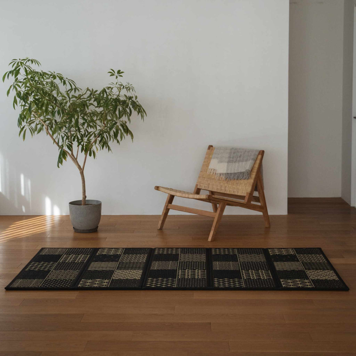 Lang sort tatami-måtte med geometriske mønstre på et stuegulv, der skaber en sofistikeret zen-indretningsatmosfære.