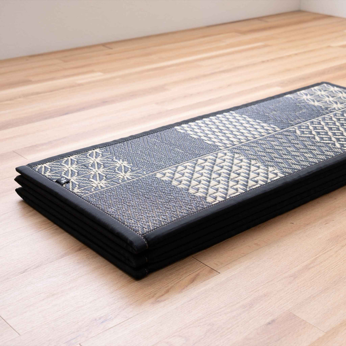 Folded black geometric tatami mat placed on a wooden floor showing its compact storage design.