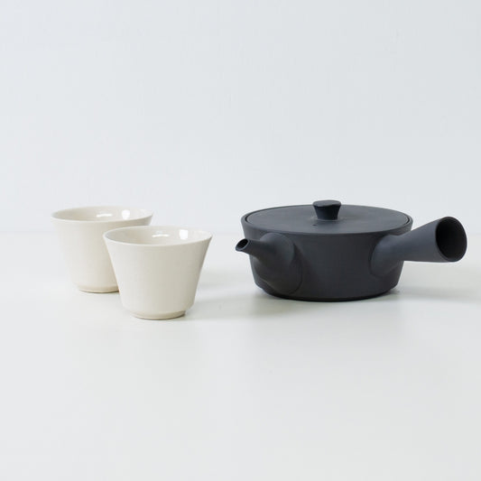 Flat black japanese teapot paired with glossy white high footed tea cups showing a contrast in texture.