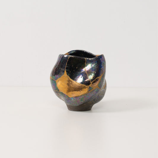 An authentic kintsugi matcha bowl stands alone highlighting colorful iridescent glazes and bold gold mends of pottery art