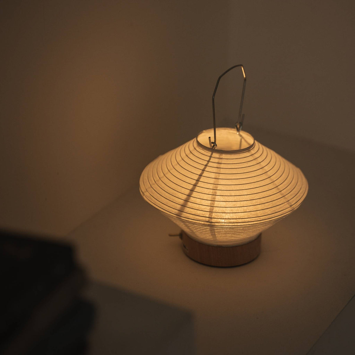 Overhead view of a lit portable lamp made of mino washi paper highlighting the ribbed structure and warm light