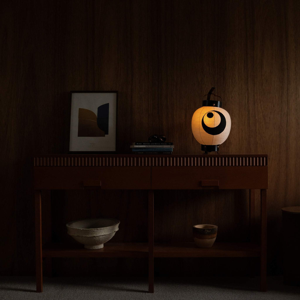 "Lampe japonaise en papier posée sur un meuble-console de style mid-century modern, ajoutant une ambiance chaleureuse à un salon."