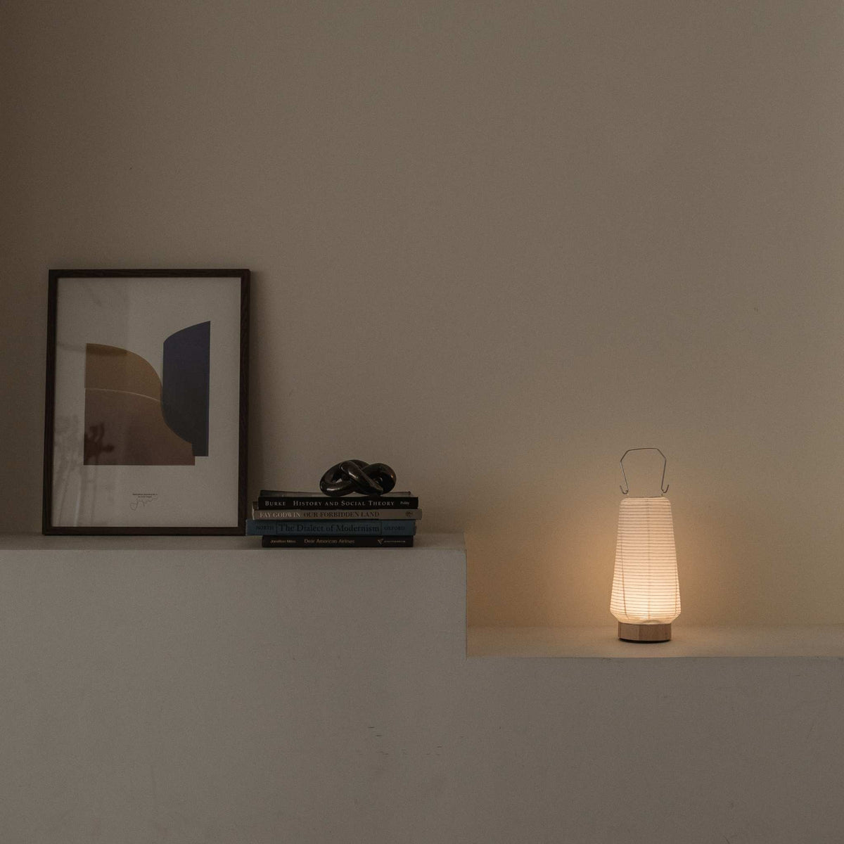 Leuchtende japanische Papier-Tischlampe RIN 04 auf einem Regal neben Büchern, die sanftes Umgebungslicht spendet und für einen Japandi-Einrichtungsstil geeignet ist