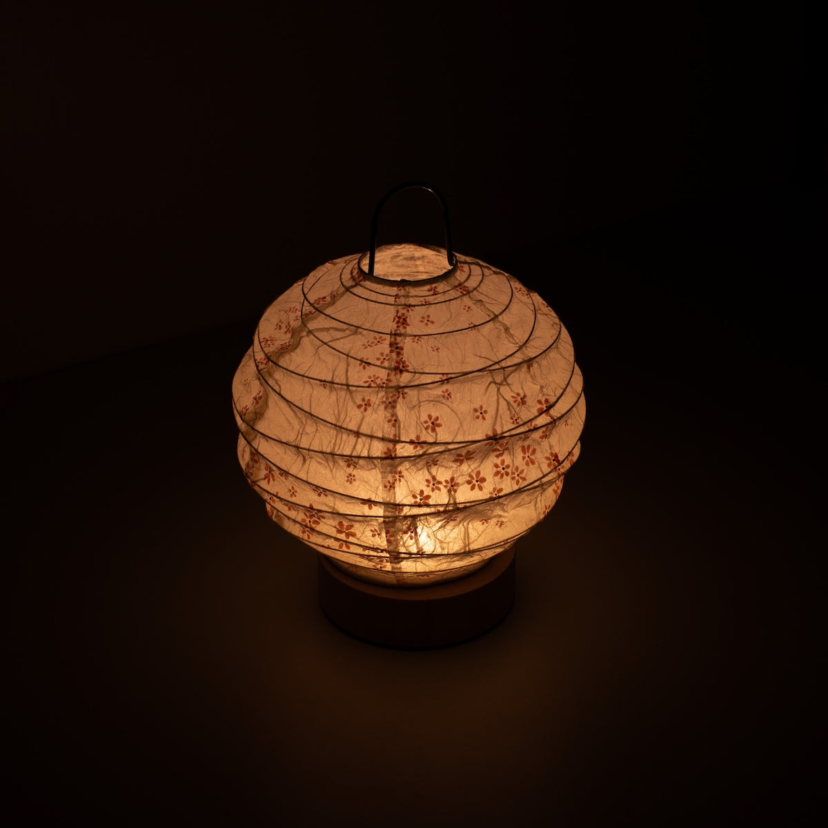 Japanese Paper Table Lamp "Yuhi" Sakura, white, Mino Washi paper - high angle view of lit Japandi style lamp with wire handle.