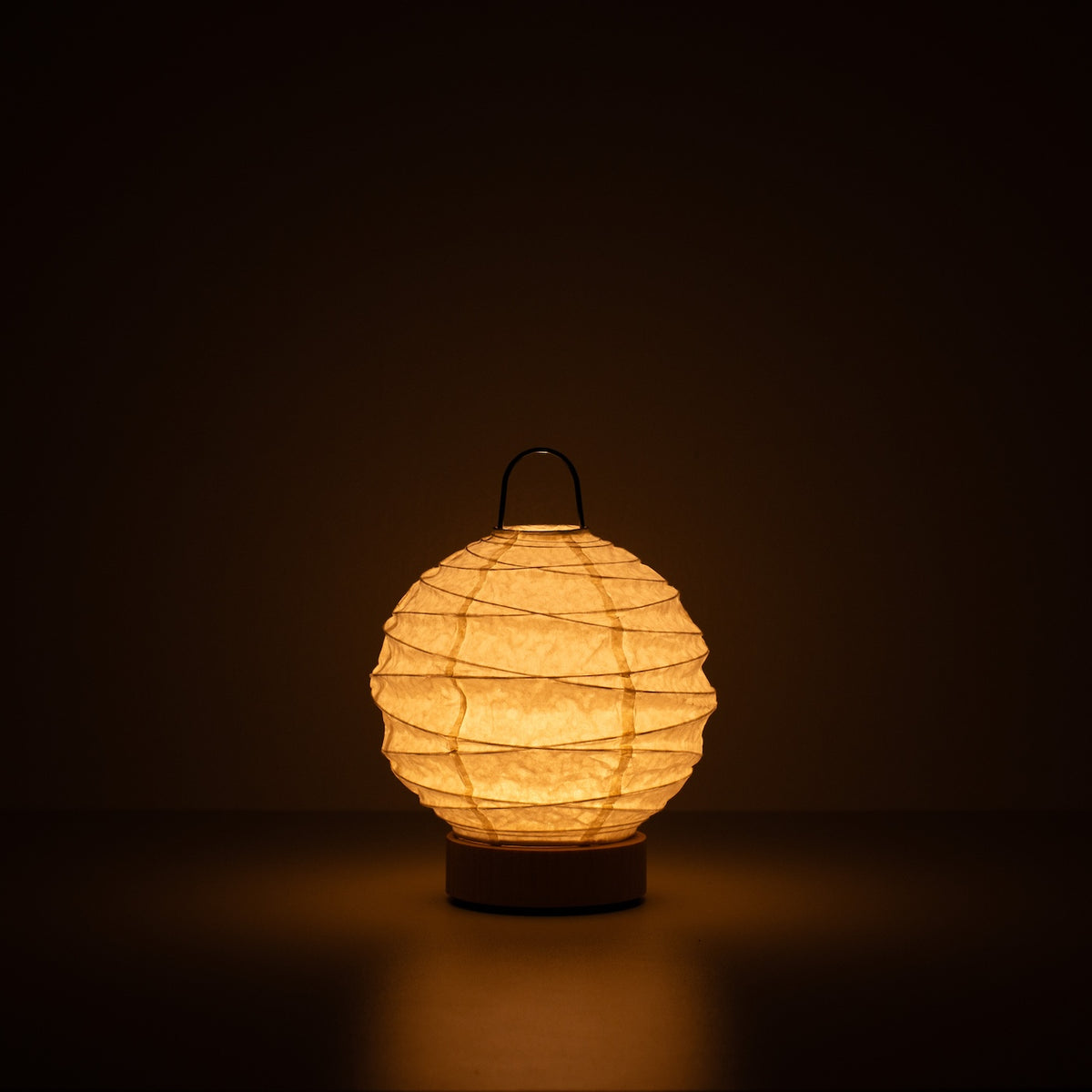 Japanese Paper Table Lamp "Yuhi", white, Mino Washi paper - lit round paper lamp casting a warm glow in a dark room.