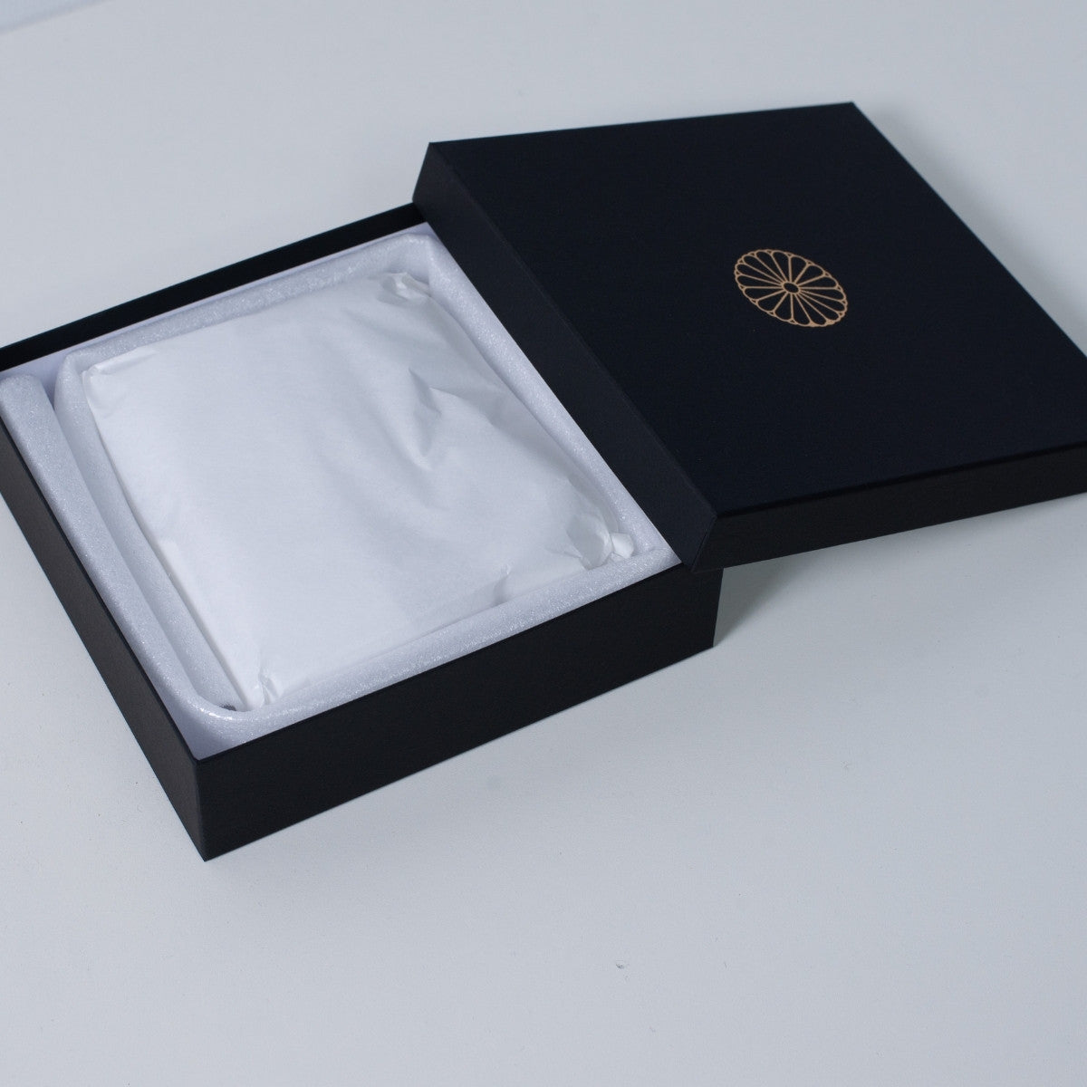 Schwarze, schmale Ninshu-Geschenkbox für japanischen Räucherstäbchenhalter aus Keramik, mit einem sicher verpackten, flachen Gefäß in weißem Packpapier.