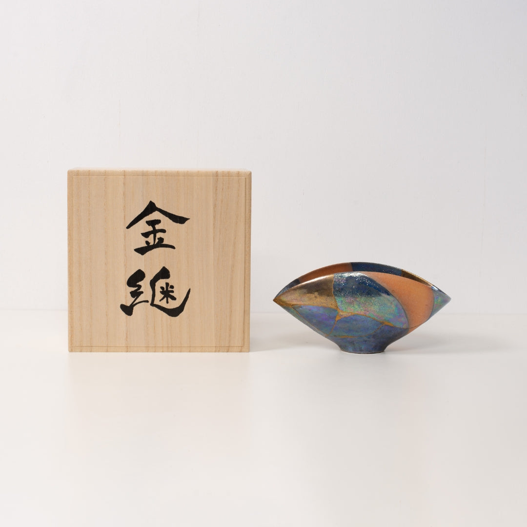 An iridescent kintsugi bowl sits next to a wooden japanese gift box showcasing meaningful wabi sabi art