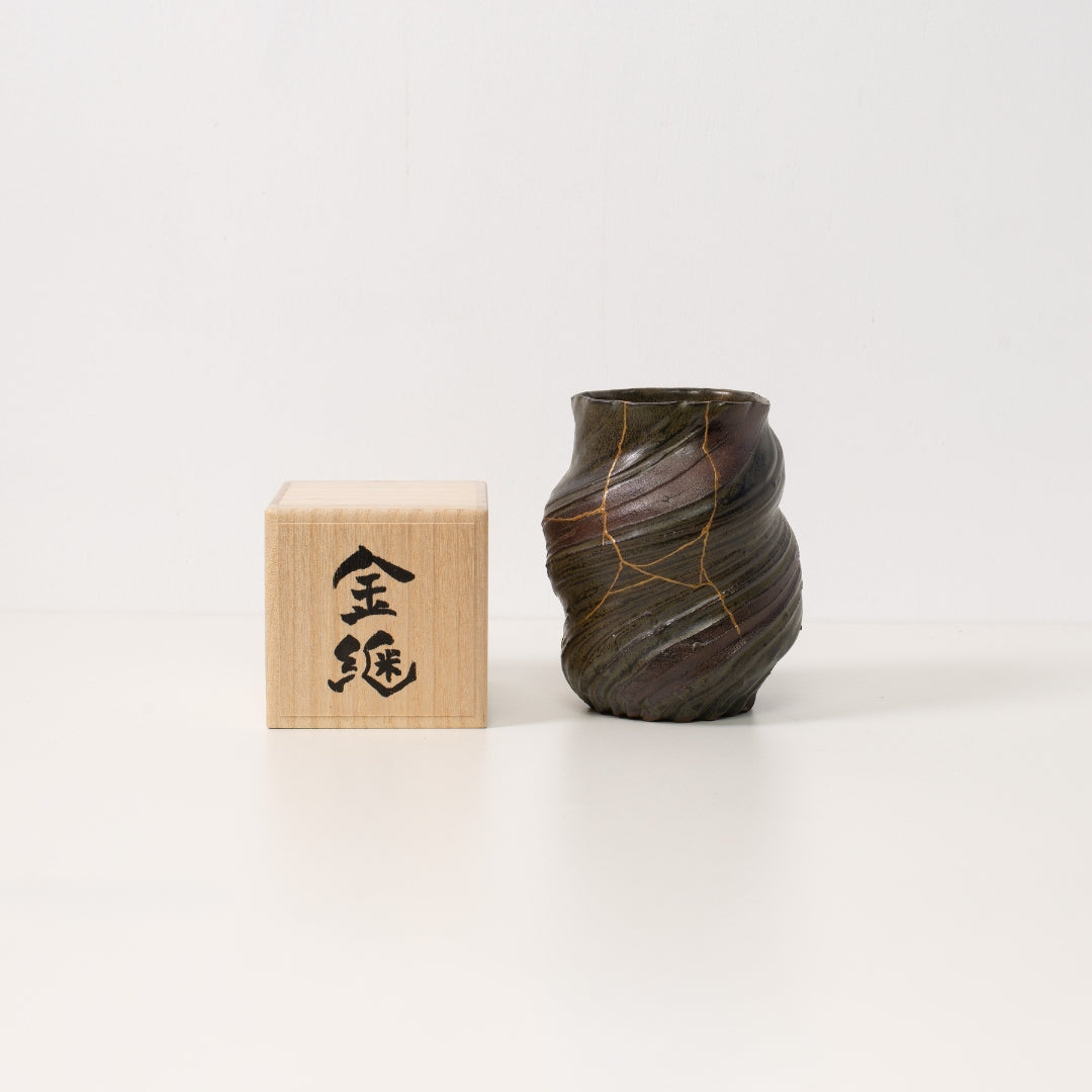 "Een donkere kintsugi-bloemenvaas staat naast een houten kist die prachtige wabi-sabi-kunst en een uniek Japans geschenk vertegenwoordigt"