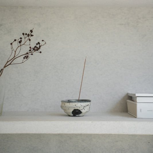 Wit en zwart Japans wierookvat op een lichte plank met boeken, wat zorgt voor een serene sfeer voor een ochtend yogasessie.