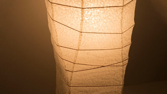 Eine Nahaufnahme des unteren Teils einer japanischen Washi-Papierlampe, von oben aufgenommen, die ihre eleganten Kurven und ihr warmes Licht zeigt