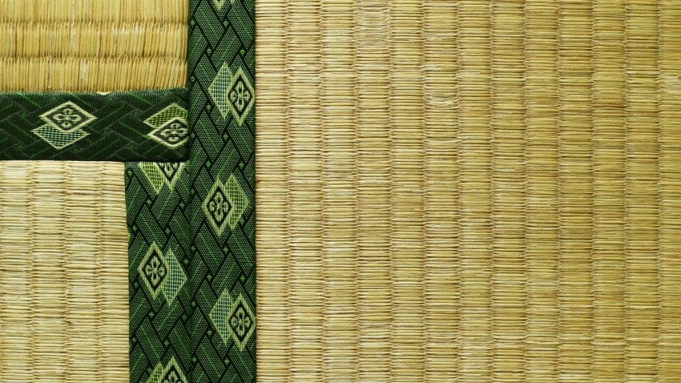Close-up van traditionele tatamimat met geweven textuur en een groene decoratieve stoffen rand met ruitpatronen.
