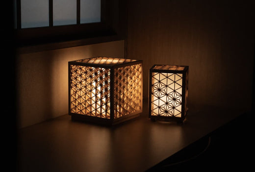 Deux lanternes Kumiko, chacune ornée d'un motif kumiko japonais complexe différent, diffusent une douce lumière dans le coin d'une pièce traditionnelle.