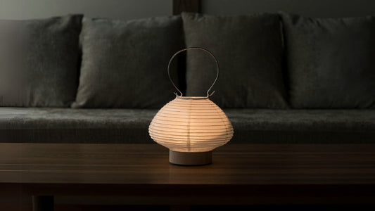 Japanese paper table lamp shaped like a lantern emitting a warm glow on a wooden table in a living room
