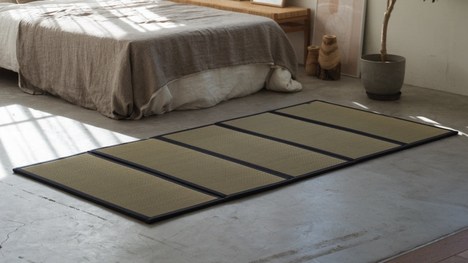Matelas tatami à cinq panneaux sur un sol de chambre en béton servant de base saine et respirante pour un futon.