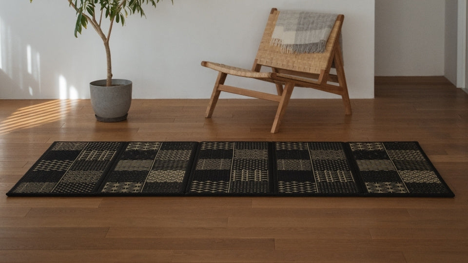 Lang sort japansk tatami-måtte med geometriske mønstre på gulvet i en japandi-stue, der skaber en sofistikeret zen-dekorationsatmosfære.