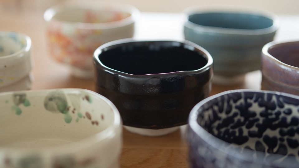 Five diverse Mino Ware Japanese matcha chawan bowls, featuring a central dark black bowl, and others with colorful glazes and patterns, ideal for tea ceremony.
